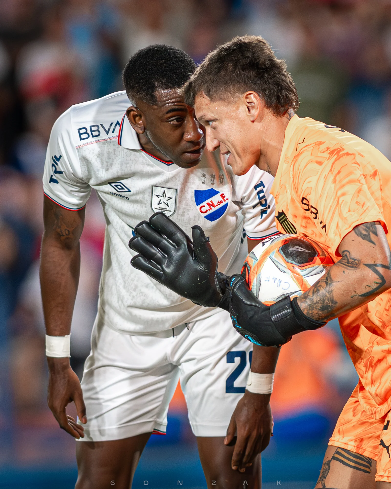 Un jugador y un arquero conversan de cerca en la cancha.