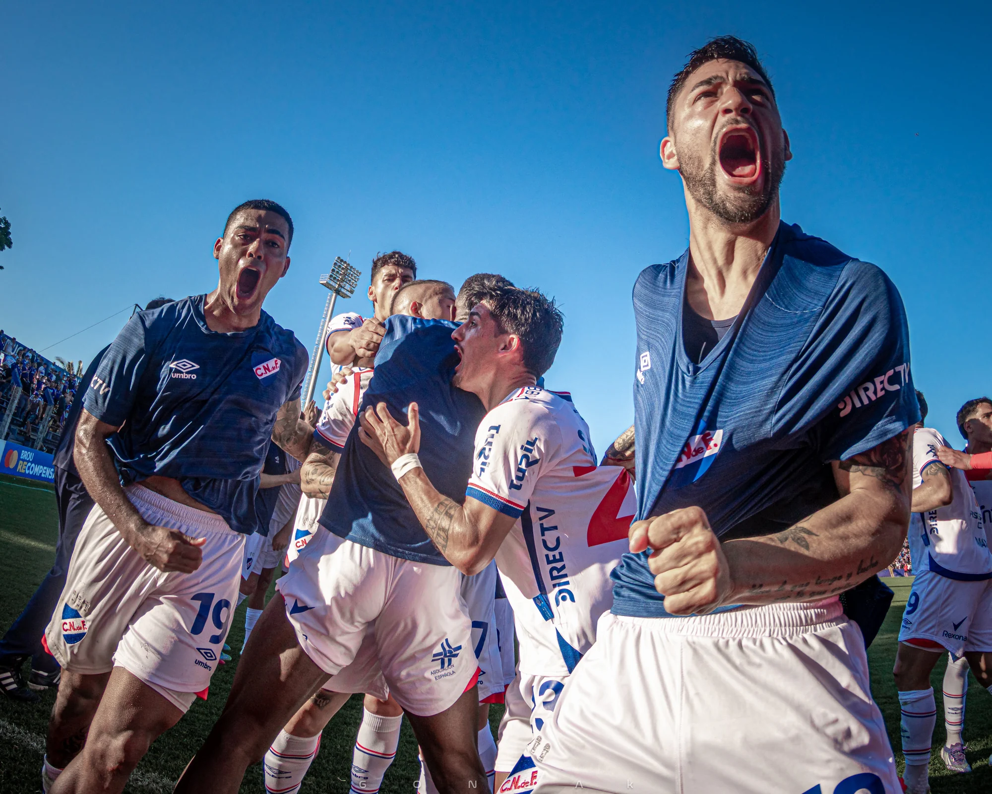 Jugadores de Nacional gritan y festejan juntos bajo el cielo azul.