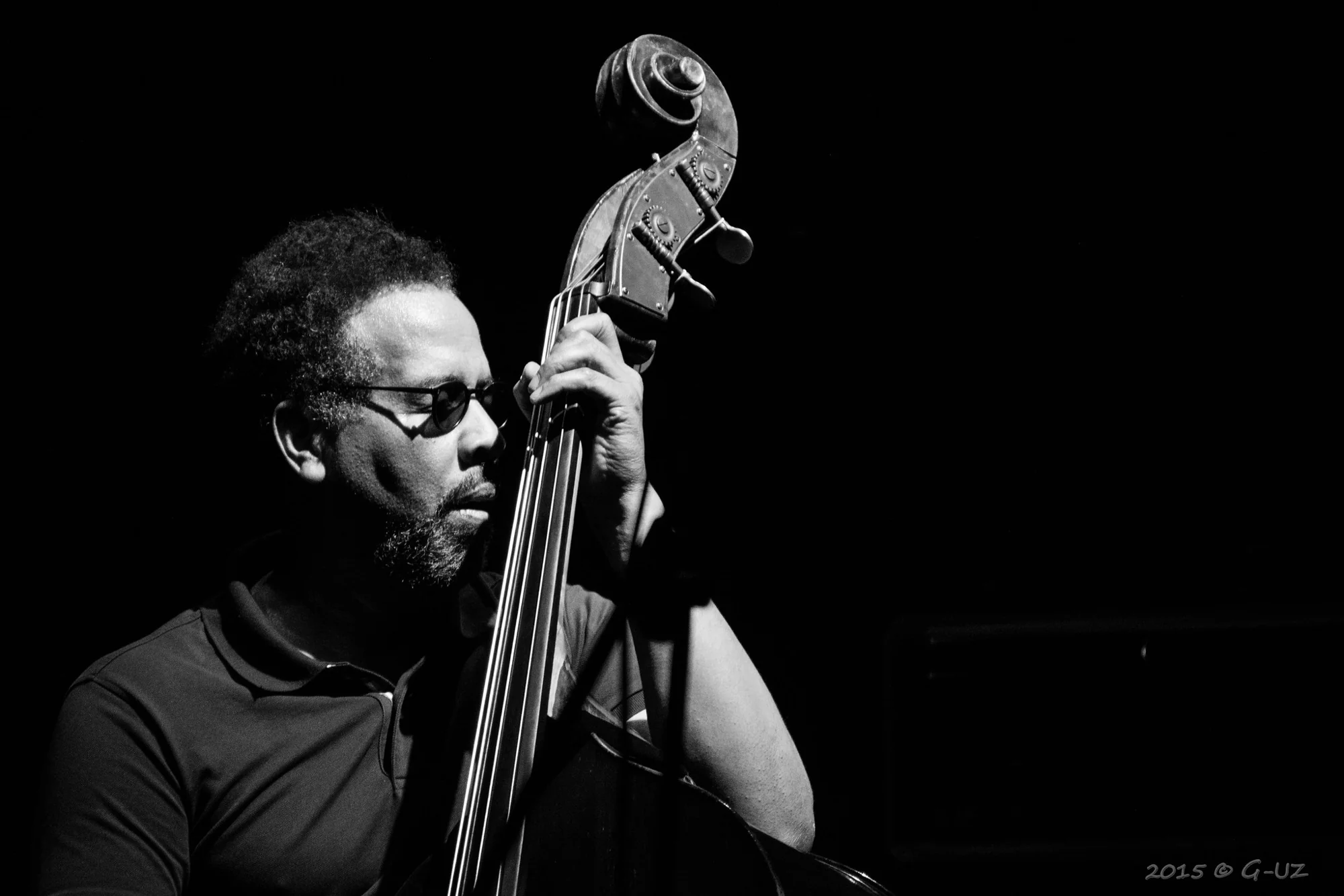 Un músico toca el contrabajo sobre un fondo negro.